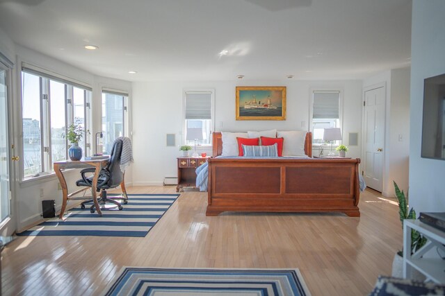 bedroom featuring a baseboard radiator, multiple windows, light wood-type flooring, and access to outside