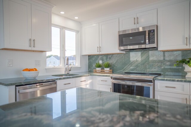 kitchen featuring appliances with stainless steel finishes, tasteful backsplash, a sink, dark stone countertops, and white cabinetry