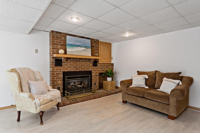 living room with a drop ceiling, a fireplace, baseboards, and light wood-style floors