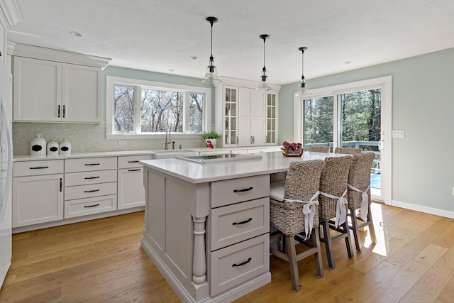 kitchen with a breakfast bar, light wood-style flooring, a sink, light countertops, and backsplash