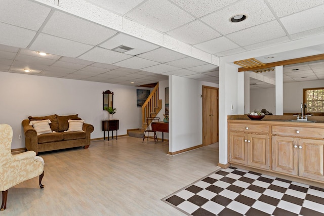 living area featuring light floors, visible vents, baseboards, a drop ceiling, and stairs