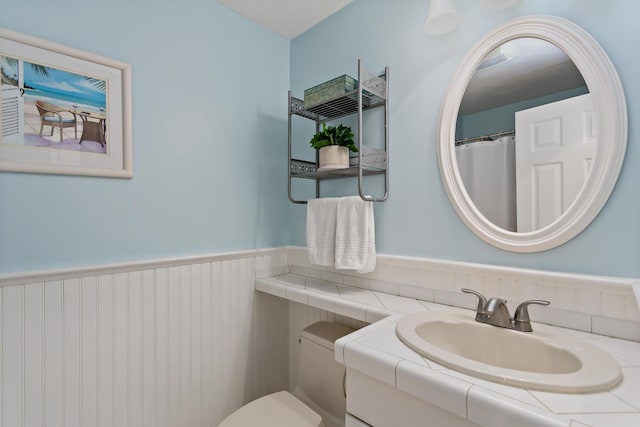 bathroom featuring a wainscoted wall, toilet, and vanity