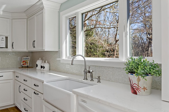 kitchen with a sink, light stone counters, backsplash, and white cabinetry