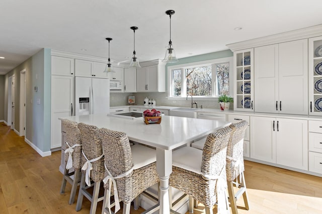 kitchen featuring a breakfast bar, a sink, white appliances, white cabinets, and light countertops