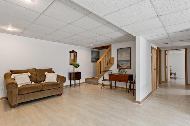 living room with light wood-type flooring, a paneled ceiling, and baseboards