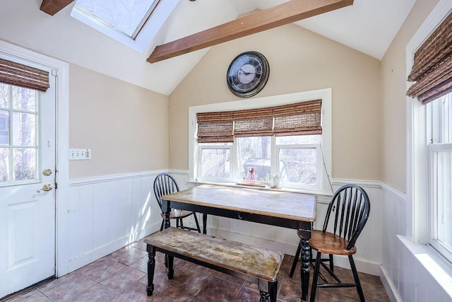 dining area featuring a healthy amount of sunlight, a wainscoted wall, and lofted ceiling with skylight