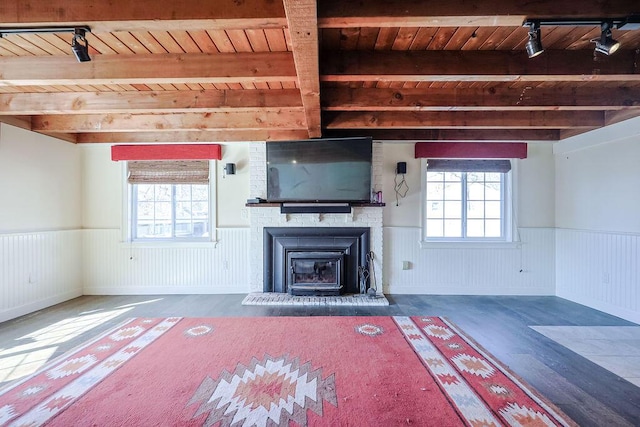 unfurnished living room featuring a wainscoted wall, a wealth of natural light, and beamed ceiling