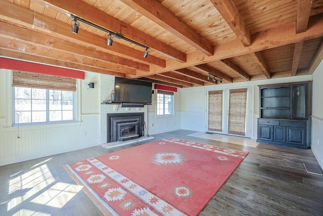 unfurnished living room with track lighting, wooden ceiling, a wainscoted wall, wood finished floors, and beam ceiling