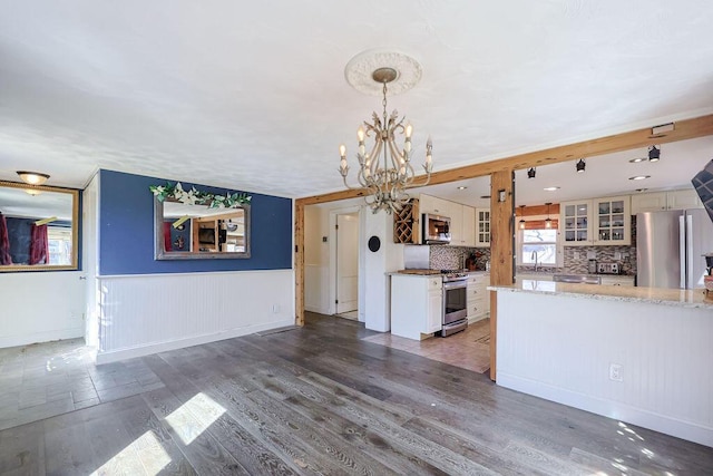 kitchen featuring wood finished floors, backsplash, appliances with stainless steel finishes, glass insert cabinets, and light stone countertops