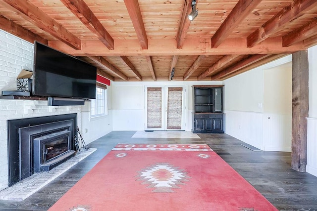 unfurnished living room with beam ceiling, rail lighting, wainscoting, wood finished floors, and wooden ceiling