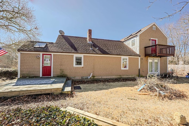 back of property with a shingled roof, a chimney, and a balcony