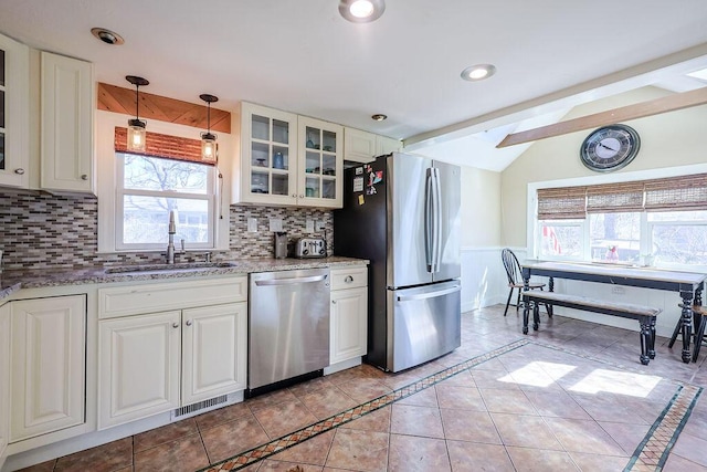 kitchen featuring tasteful backsplash, light stone counters, vaulted ceiling with beams, stainless steel appliances, and a sink