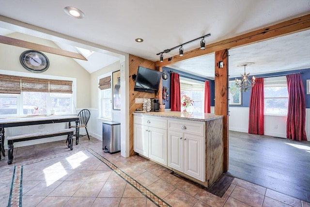 kitchen with light tile patterned floors, lofted ceiling with skylight, white cabinets, a chandelier, and baseboards