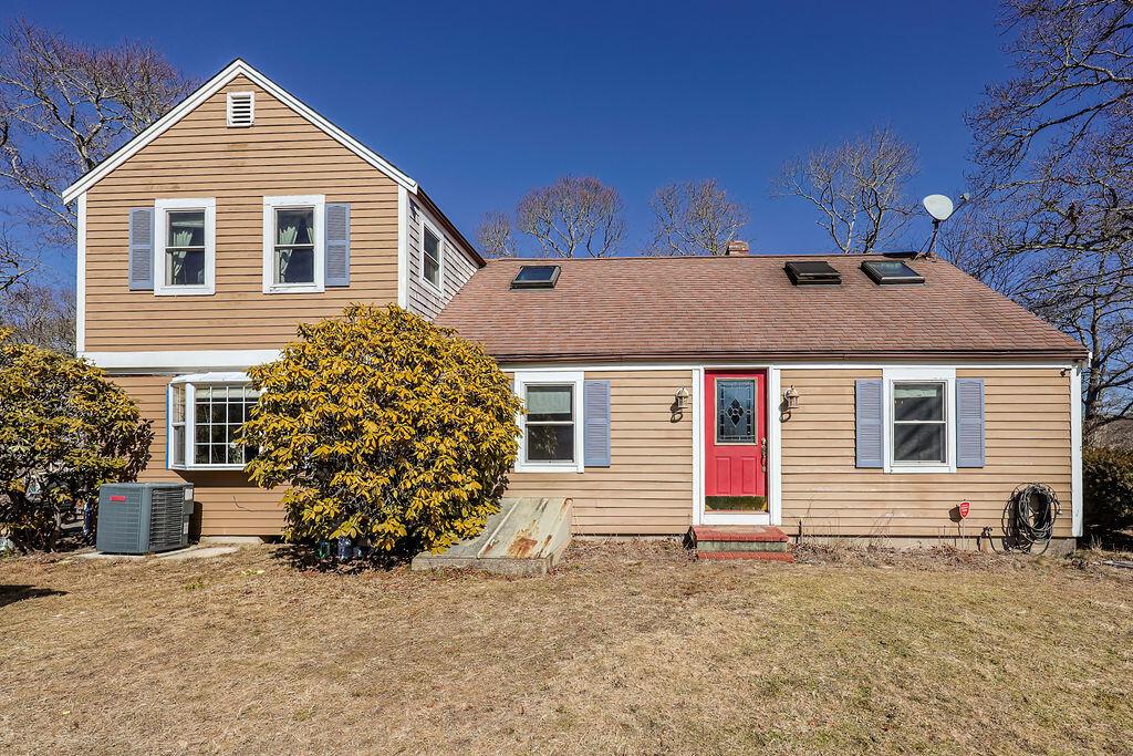 view of front of house with a shingled roof, cooling unit, and a front yard