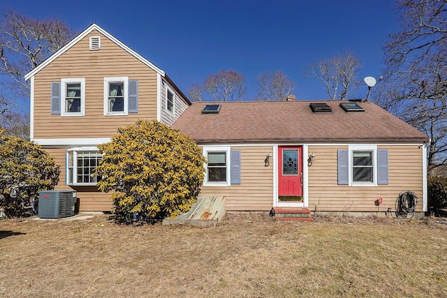 view of front of house with a shingled roof, cooling unit, and a front yard