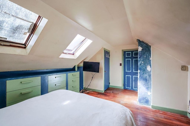 bedroom featuring vaulted ceiling with skylight, baseboards, and wood finished floors