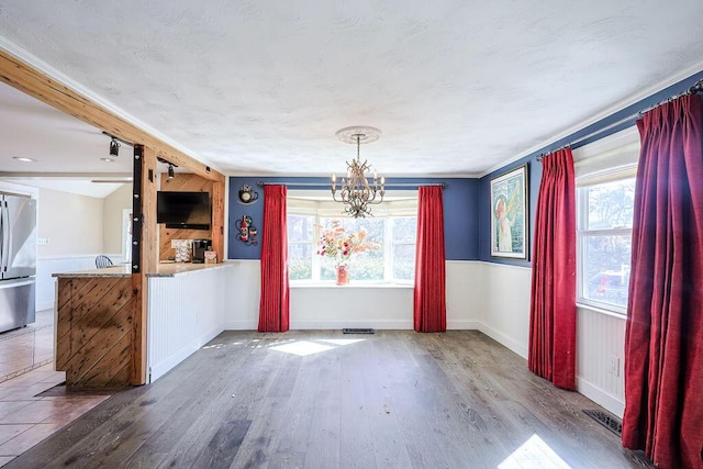 unfurnished dining area with a chandelier, a healthy amount of sunlight, baseboards, and wood finished floors