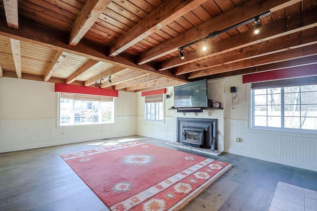 unfurnished living room with a fireplace with raised hearth, wood ceiling, wainscoting, beamed ceiling, and hardwood / wood-style floors