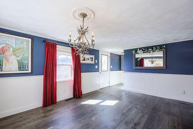 unfurnished dining area featuring a wainscoted wall, visible vents, wood finished floors, and an inviting chandelier