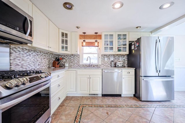 kitchen featuring light tile patterned floors, tasteful backsplash, appliances with stainless steel finishes, light stone counters, and a sink