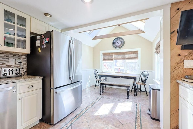 kitchen featuring lofted ceiling with beams, appliances with stainless steel finishes, glass insert cabinets, light stone countertops, and backsplash