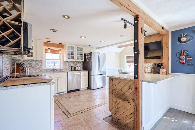 kitchen featuring light tile patterned floors, stainless steel appliances, a sink, tasteful backsplash, and glass insert cabinets