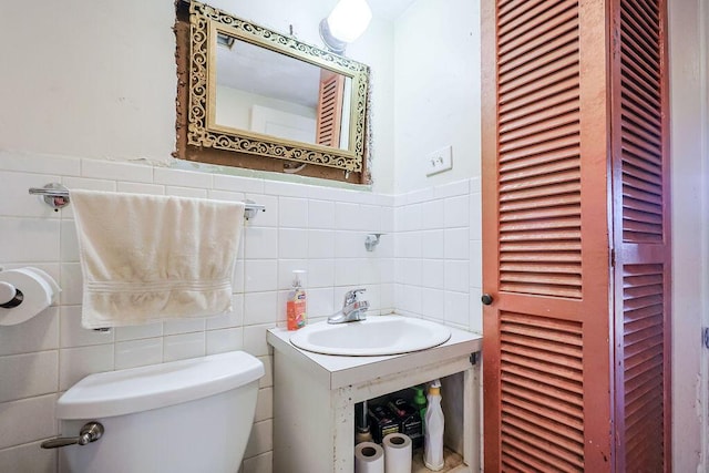 bathroom featuring wainscoting, a sink, tile walls, and toilet