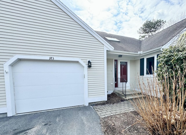 view of exterior entry featuring a garage and roof with shingles