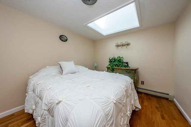 bedroom with a skylight, baseboard heating, and wood-type flooring