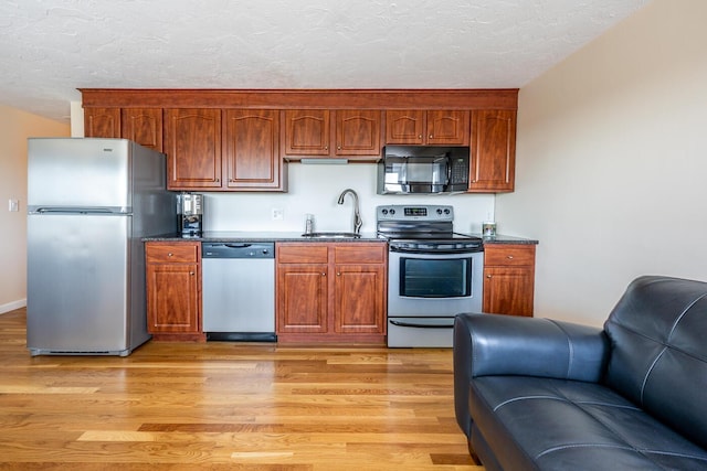 kitchen with light wood-type flooring, appliances with stainless steel finishes, a textured ceiling, and sink