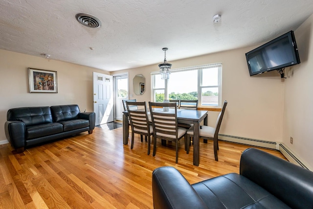 dining room featuring a notable chandelier, light hardwood / wood-style flooring, baseboard heating, and a textured ceiling