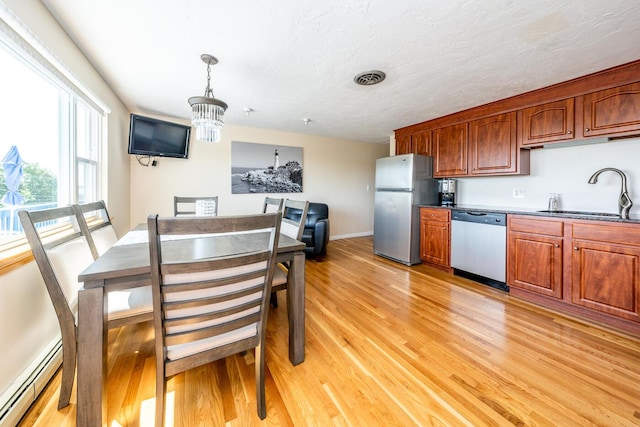 kitchen featuring appliances with stainless steel finishes, a baseboard heating unit, sink, decorative light fixtures, and light wood-type flooring