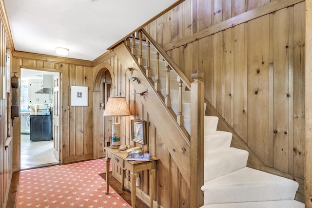 stairway featuring carpet floors, arched walkways, and wooden walls