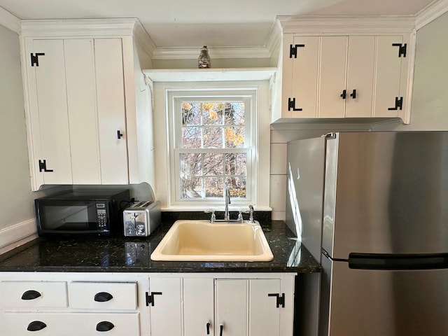 kitchen with white cabinetry, black microwave, a sink, and freestanding refrigerator