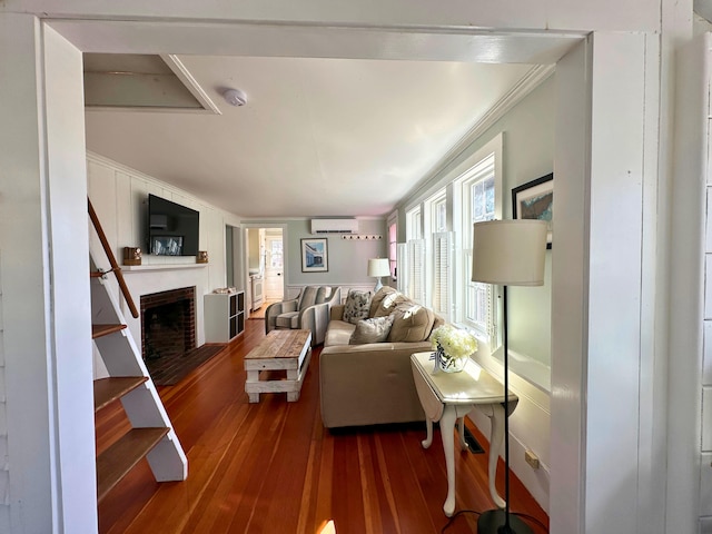 living area with a brick fireplace, wood-type flooring, a wall mounted air conditioner, and crown molding