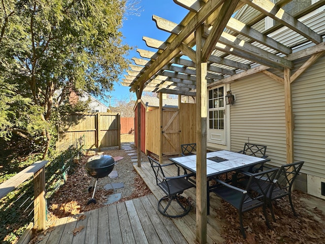 wooden deck featuring an outbuilding, fence, a shed, a pergola, and outdoor dining space