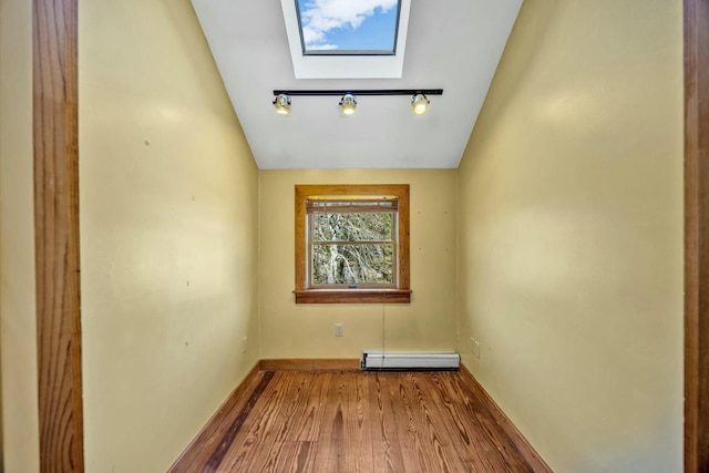 empty room featuring lofted ceiling with skylight, track lighting, a baseboard heating unit, and wood finished floors