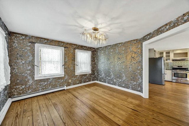 unfurnished room with a baseboard radiator, baseboards, wood-type flooring, and a chandelier