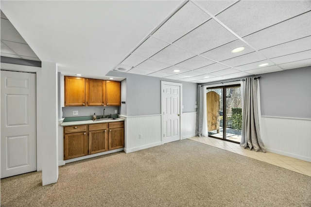 kitchen with brown cabinets, light countertops, light colored carpet, wainscoting, and a sink