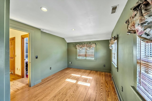 empty room featuring baseboards, visible vents, vaulted ceiling, and wood finished floors