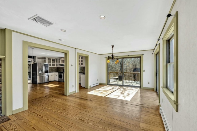 empty room with a baseboard heating unit, visible vents, baseboard heating, and wood finished floors