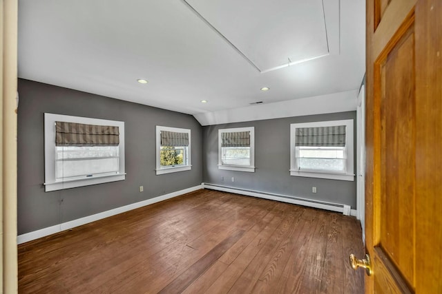 empty room featuring hardwood / wood-style flooring, a baseboard heating unit, baseboards, vaulted ceiling, and attic access