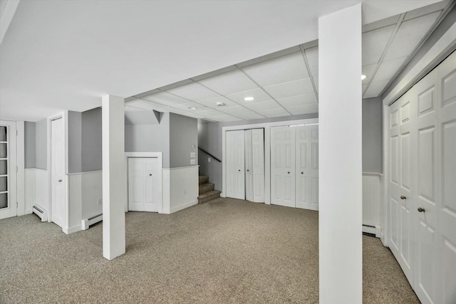 finished basement featuring stairway, a baseboard radiator, carpet flooring, and a paneled ceiling