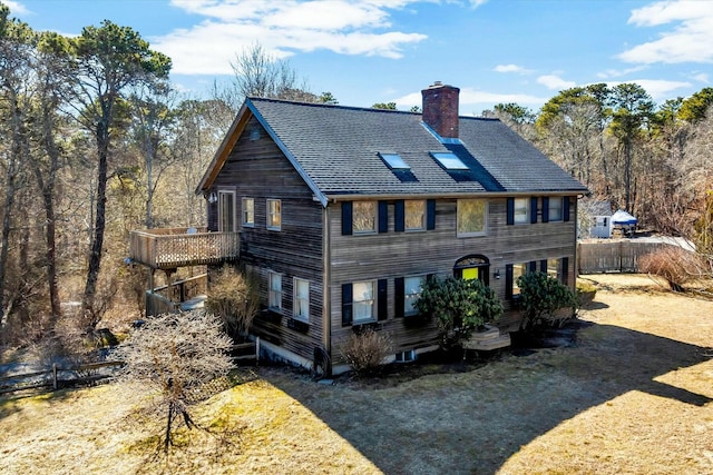 view of front facade with a shingled roof, a chimney, and fence