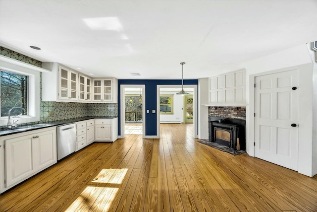 kitchen featuring dark countertops, backsplash, stainless steel dishwasher, glass insert cabinets, and a sink