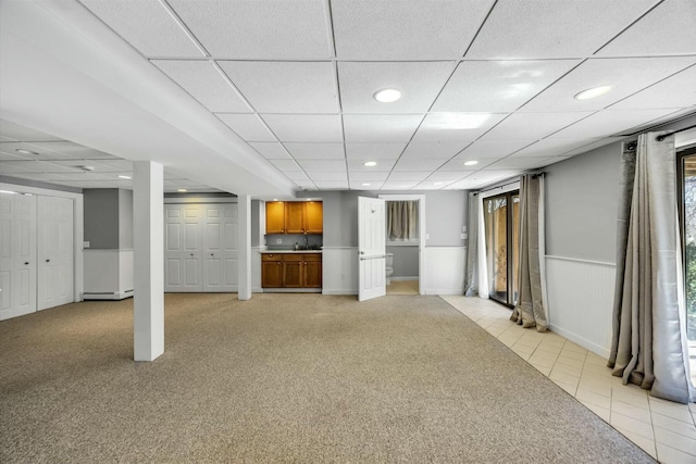 basement featuring light carpet, recessed lighting, a paneled ceiling, and wainscoting