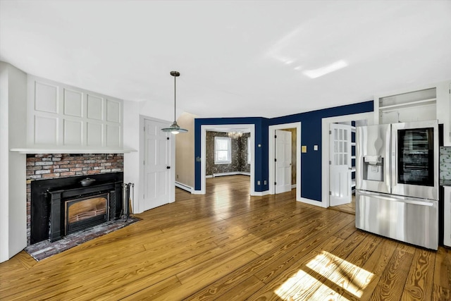 kitchen with baseboards, white cabinets, wood finished floors, a fireplace, and stainless steel refrigerator with ice dispenser