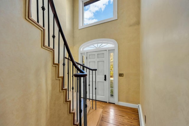 entrance foyer with light wood finished floors, baseboards, a towering ceiling, a baseboard radiator, and stairs