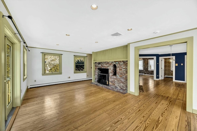 unfurnished living room with a baseboard radiator, visible vents, light wood-style floors, a brick fireplace, and crown molding