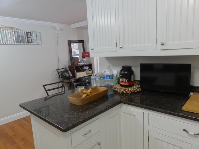 kitchen with white cabinets, dark stone counters, light hardwood / wood-style flooring, and crown molding